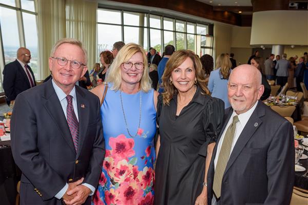 Four people dressed in business professional clothing smile at the camera. 